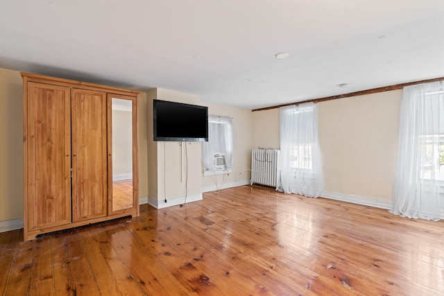 unfurnished living room featuring radiator heating unit, cooling unit, and light hardwood / wood-style floors