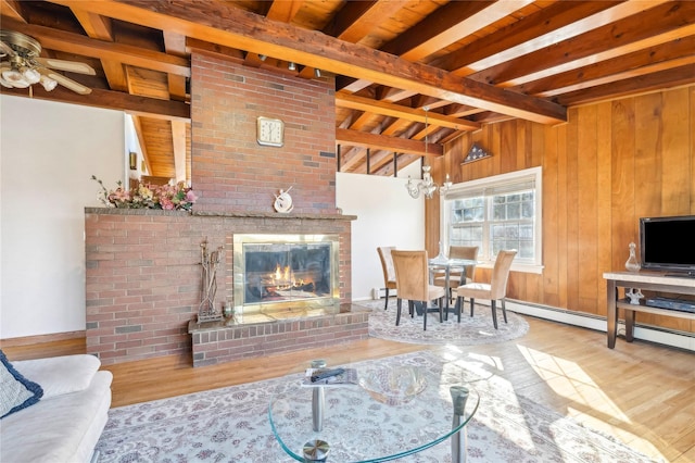 living room featuring a brick fireplace, beamed ceiling, wood walls, light hardwood / wood-style floors, and ceiling fan with notable chandelier