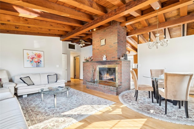 living room featuring lofted ceiling with beams, wood ceiling, ceiling fan with notable chandelier, and a brick fireplace