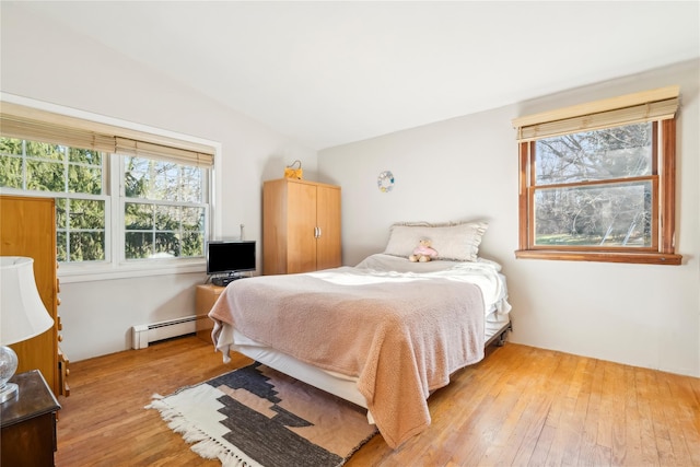 bedroom with baseboard heating, light hardwood / wood-style floors, and lofted ceiling