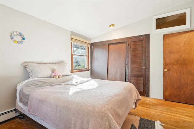 bedroom with wood-type flooring, baseboard heating, a closet, and lofted ceiling