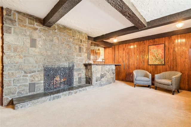 unfurnished room with carpet flooring, beam ceiling, a fireplace, and wooden walls