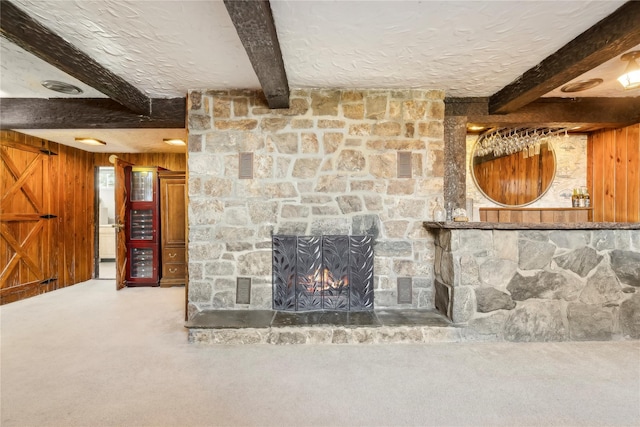 unfurnished living room featuring beamed ceiling, a stone fireplace, carpet floors, and wooden walls