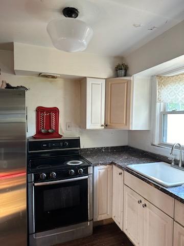 kitchen with dark countertops, stainless steel fridge, black range with electric cooktop, and a sink