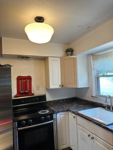 kitchen featuring a sink, range with electric cooktop, white cabinetry, dark countertops, and stainless steel fridge