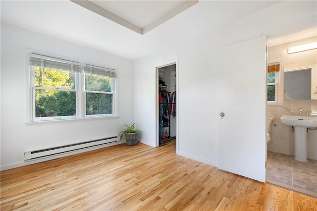 unfurnished bedroom with ensuite bath, baseboard heating, a walk in closet, a closet, and light wood-type flooring