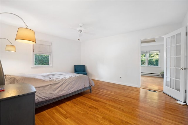 bedroom with ceiling fan, hardwood / wood-style floors, and a baseboard heating unit