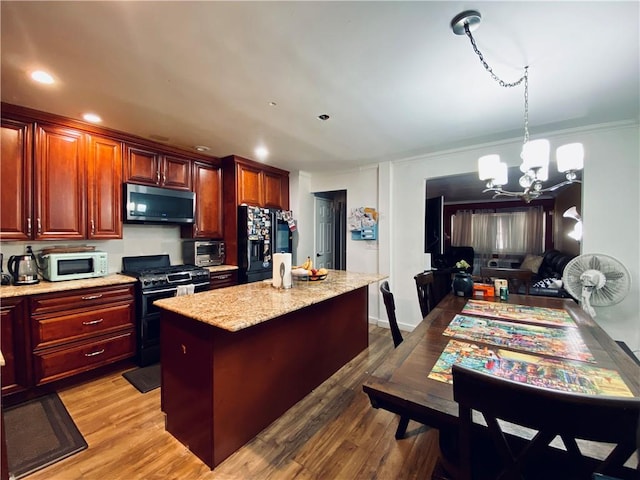 kitchen with a chandelier, pendant lighting, wood-type flooring, a kitchen island, and black appliances