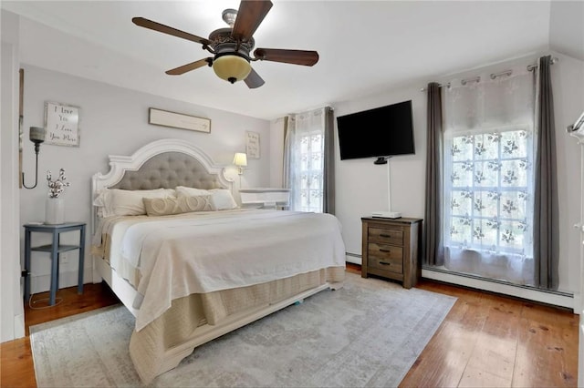 bedroom with multiple windows, wood-type flooring, baseboard heating, and ceiling fan