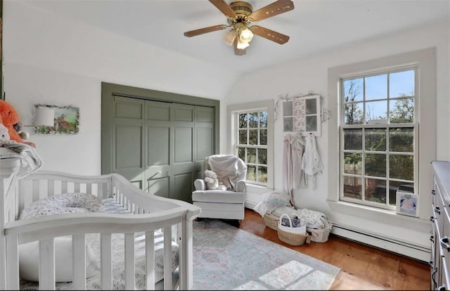 bedroom with ceiling fan, a baseboard radiator, vaulted ceiling, a crib, and hardwood / wood-style flooring