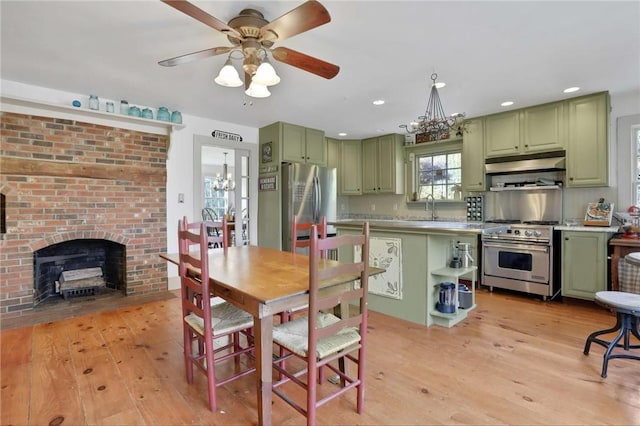 kitchen with a brick fireplace, stainless steel appliances, sink, light hardwood / wood-style floors, and green cabinets