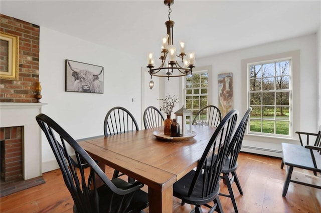 dining area featuring light wood-type flooring, a brick fireplace, a wealth of natural light, and a notable chandelier