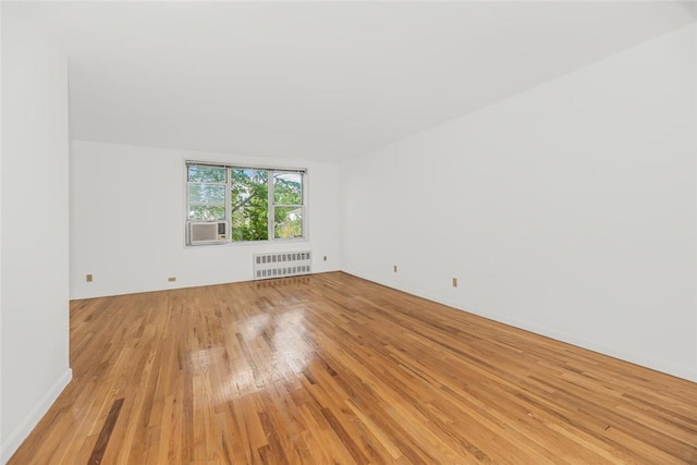 unfurnished room with cooling unit, radiator heating unit, and light wood-type flooring