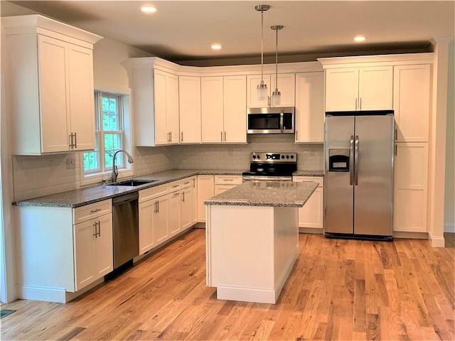 kitchen with appliances with stainless steel finishes, dark stone counters, sink, decorative light fixtures, and a kitchen island