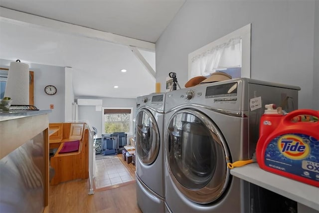 clothes washing area featuring light wood-type flooring, separate washer and dryer, and a wall unit AC