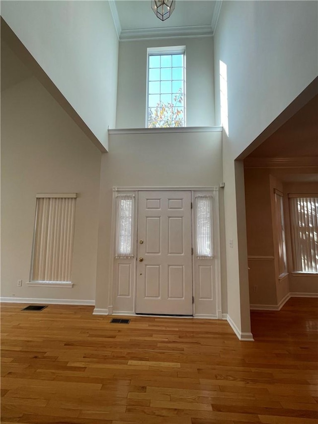 entrance foyer with a high ceiling, light hardwood / wood-style floors, and crown molding