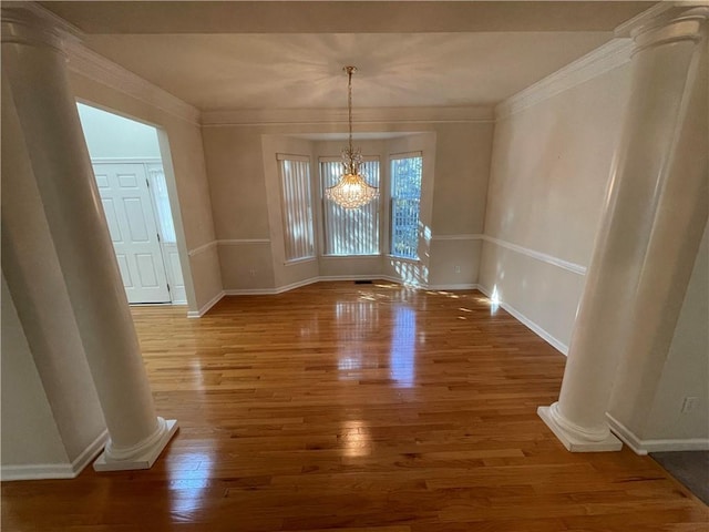 unfurnished dining area with ornate columns, a chandelier, crown molding, and dark wood-type flooring