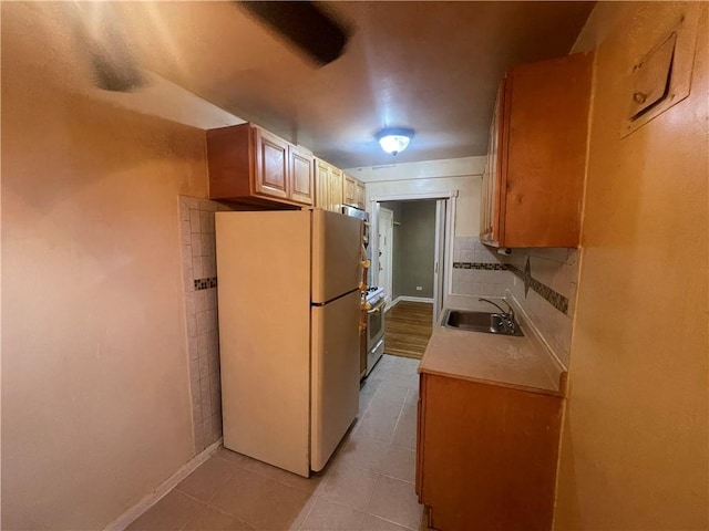 kitchen with decorative backsplash, sink, light tile patterned floors, stainless steel range oven, and white fridge