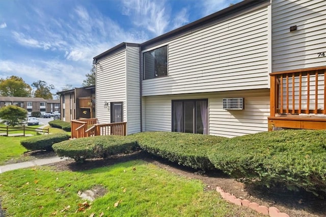 view of side of property featuring a yard, a wall unit AC, and a deck