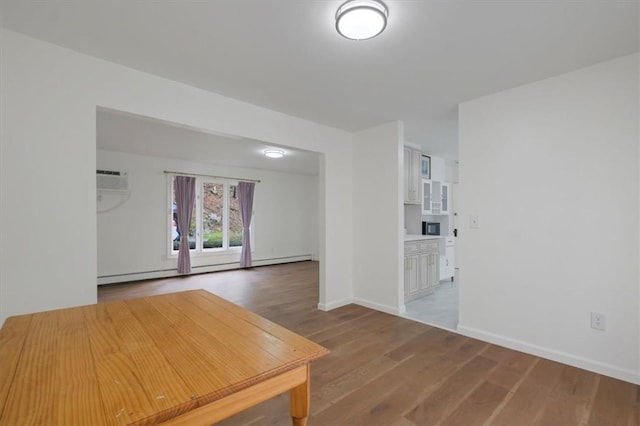 empty room featuring a wall mounted AC, wood-type flooring, and baseboard heating