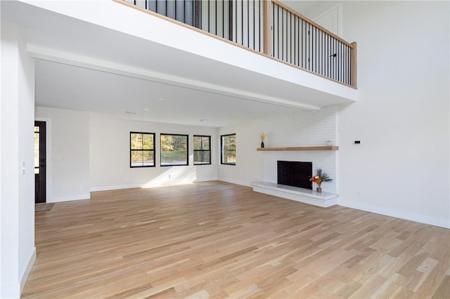 unfurnished living room featuring a brick fireplace, a towering ceiling, and light hardwood / wood-style flooring