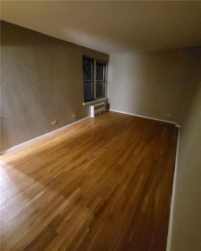 spare room with radiator heating unit, wood finished floors, and baseboards