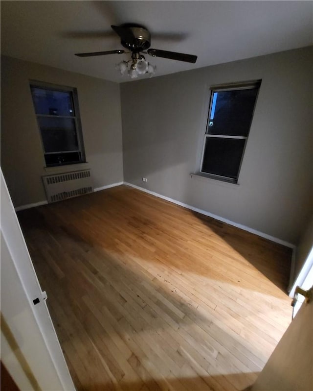 empty room with baseboards, ceiling fan, wood finished floors, and radiator