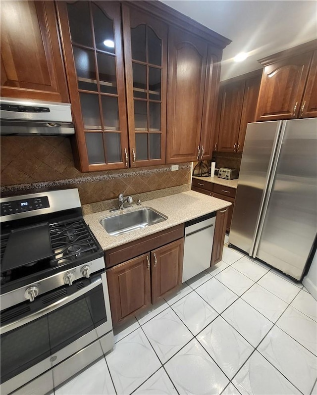 kitchen with glass insert cabinets, stainless steel appliances, light countertops, under cabinet range hood, and a sink