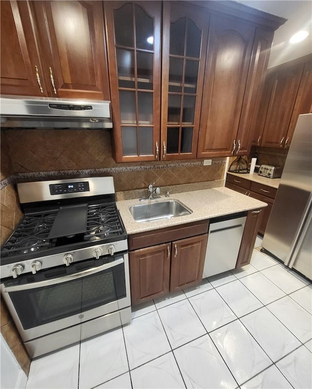 kitchen with glass insert cabinets, appliances with stainless steel finishes, light countertops, under cabinet range hood, and a sink