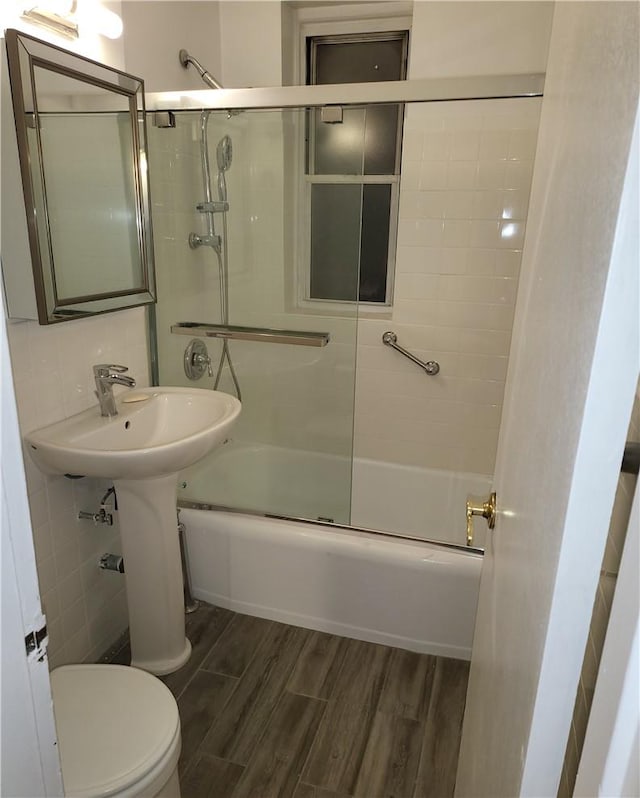 bathroom featuring tile walls, toilet, wood finished floors, combined bath / shower with glass door, and backsplash