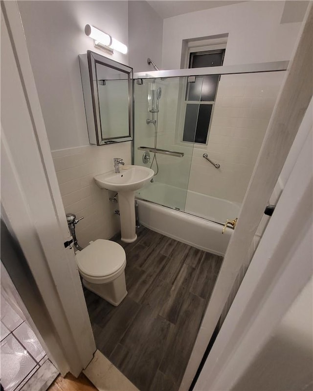 full bath featuring combined bath / shower with glass door, wood finished floors, and toilet