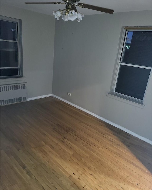 empty room featuring baseboards, ceiling fan, radiator heating unit, and wood finished floors