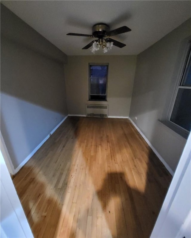 unfurnished living room with ceiling fan, radiator heating unit, wood finished floors, and baseboards