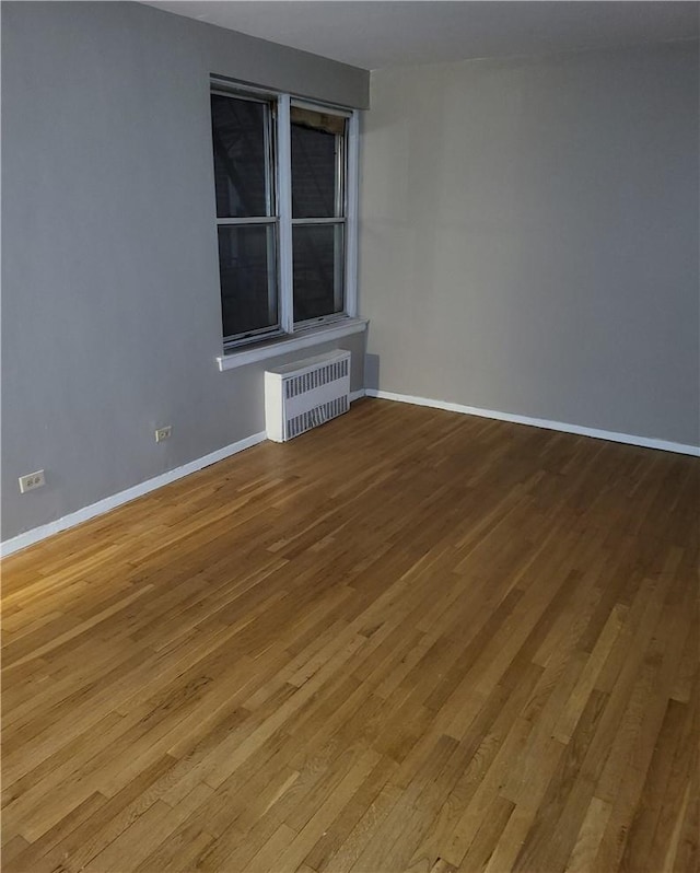 unfurnished room with radiator heating unit, light wood-style flooring, and baseboards