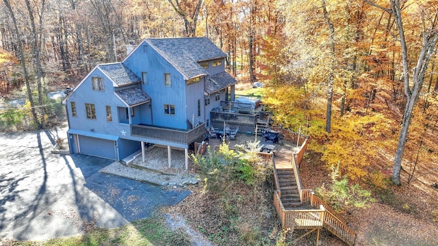 exterior space featuring a garage, stairs, driveway, roof with shingles, and a wooded view