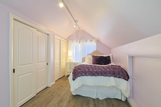 bedroom featuring vaulted ceiling, two closets, track lighting, and wood finished floors