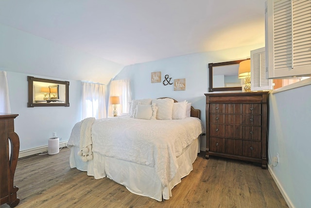 bedroom with a baseboard heating unit, baseboards, vaulted ceiling, and wood finished floors