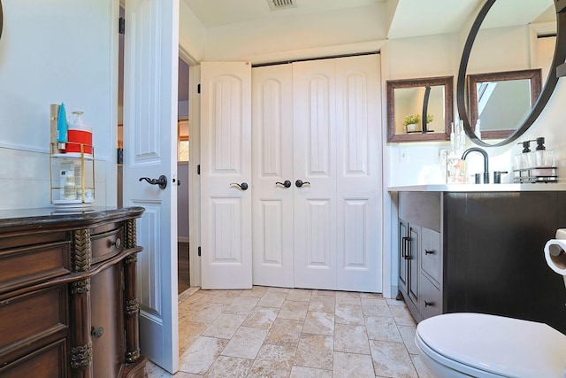 bathroom featuring toilet, stone finish floor, visible vents, and vanity