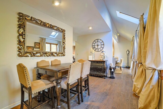 dining space featuring lofted ceiling with skylight, wood finished floors, and baseboards