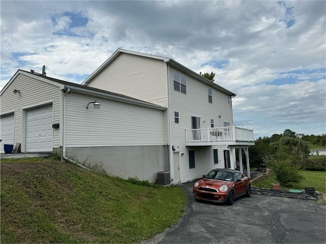 exterior space featuring a balcony, a garage, cooling unit, and a lawn