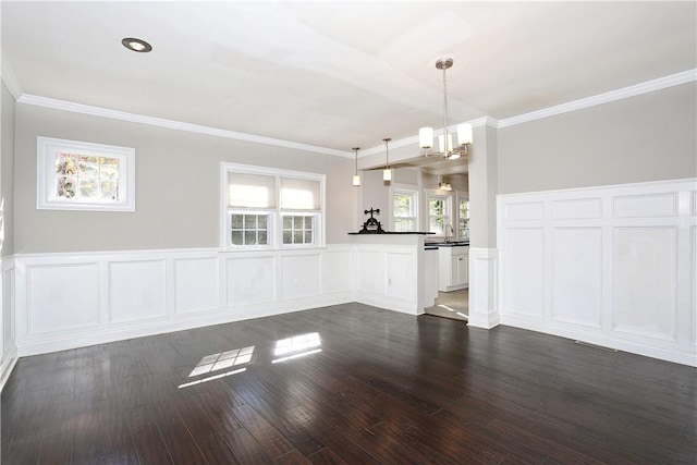 unfurnished living room with dark hardwood / wood-style floors, an inviting chandelier, crown molding, and sink