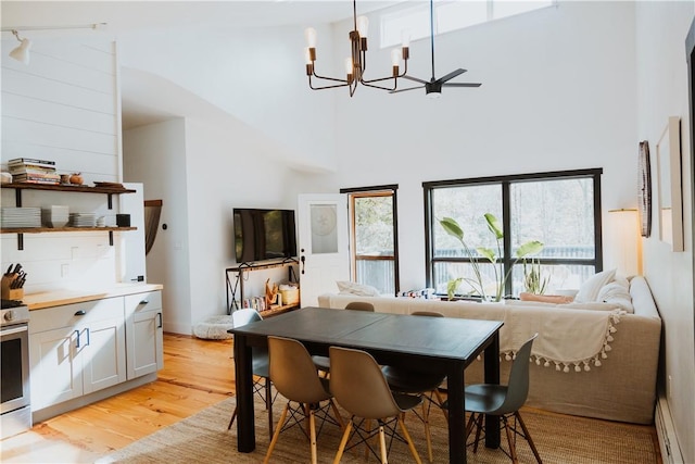 dining space with ceiling fan with notable chandelier, a high ceiling, and light wood-type flooring