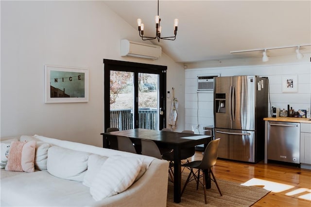 dining space with lofted ceiling, wood-type flooring, an AC wall unit, and an inviting chandelier