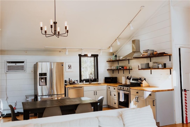 kitchen featuring appliances with stainless steel finishes, exhaust hood, sink, an AC wall unit, and hanging light fixtures