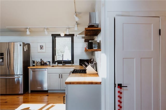 kitchen with sink, rail lighting, light wood-type flooring, appliances with stainless steel finishes, and butcher block countertops