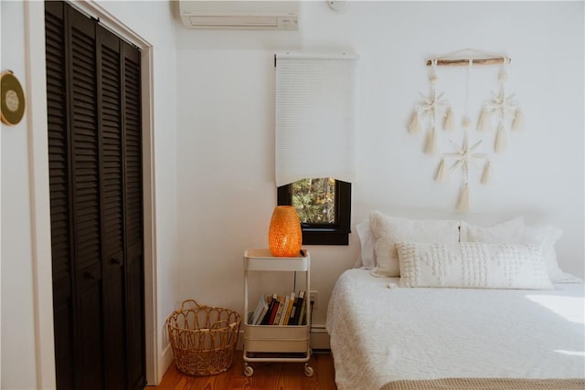 bedroom with a closet, wood-type flooring, and a wall mounted AC