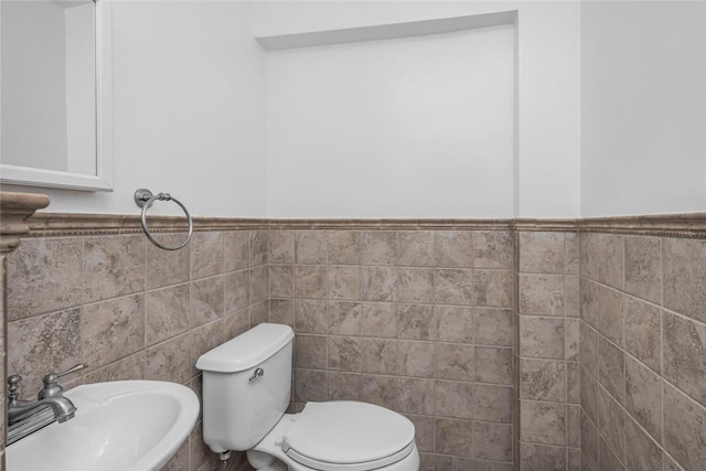 bathroom featuring toilet, tile walls, and sink