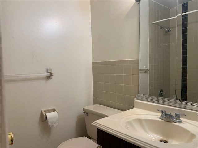 bathroom with a tile shower, vanity, tile walls, and toilet