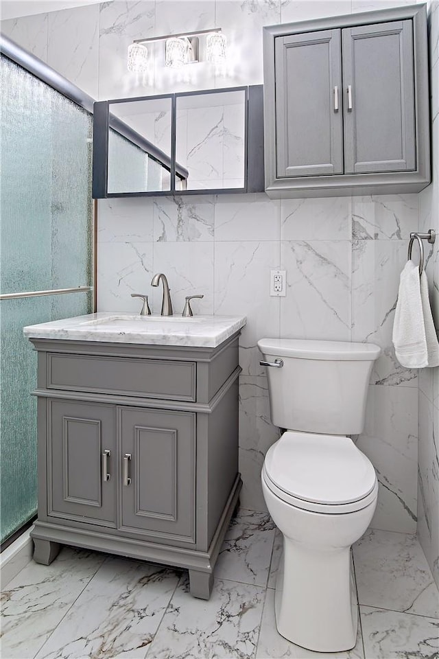 bathroom with vanity, a shower with door, toilet, and tile walls