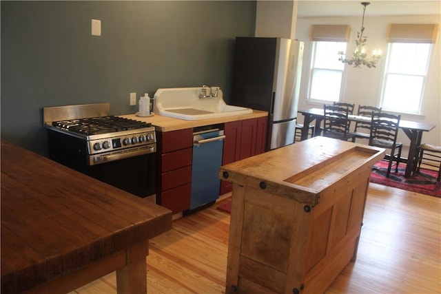 kitchen featuring an inviting chandelier, sink, light wood-type flooring, decorative light fixtures, and stainless steel appliances